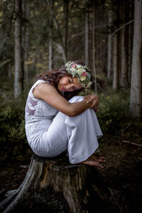 Young woman holding tree trunk in forest