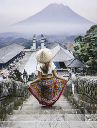 Rear view of woman walking by buildings against mountains