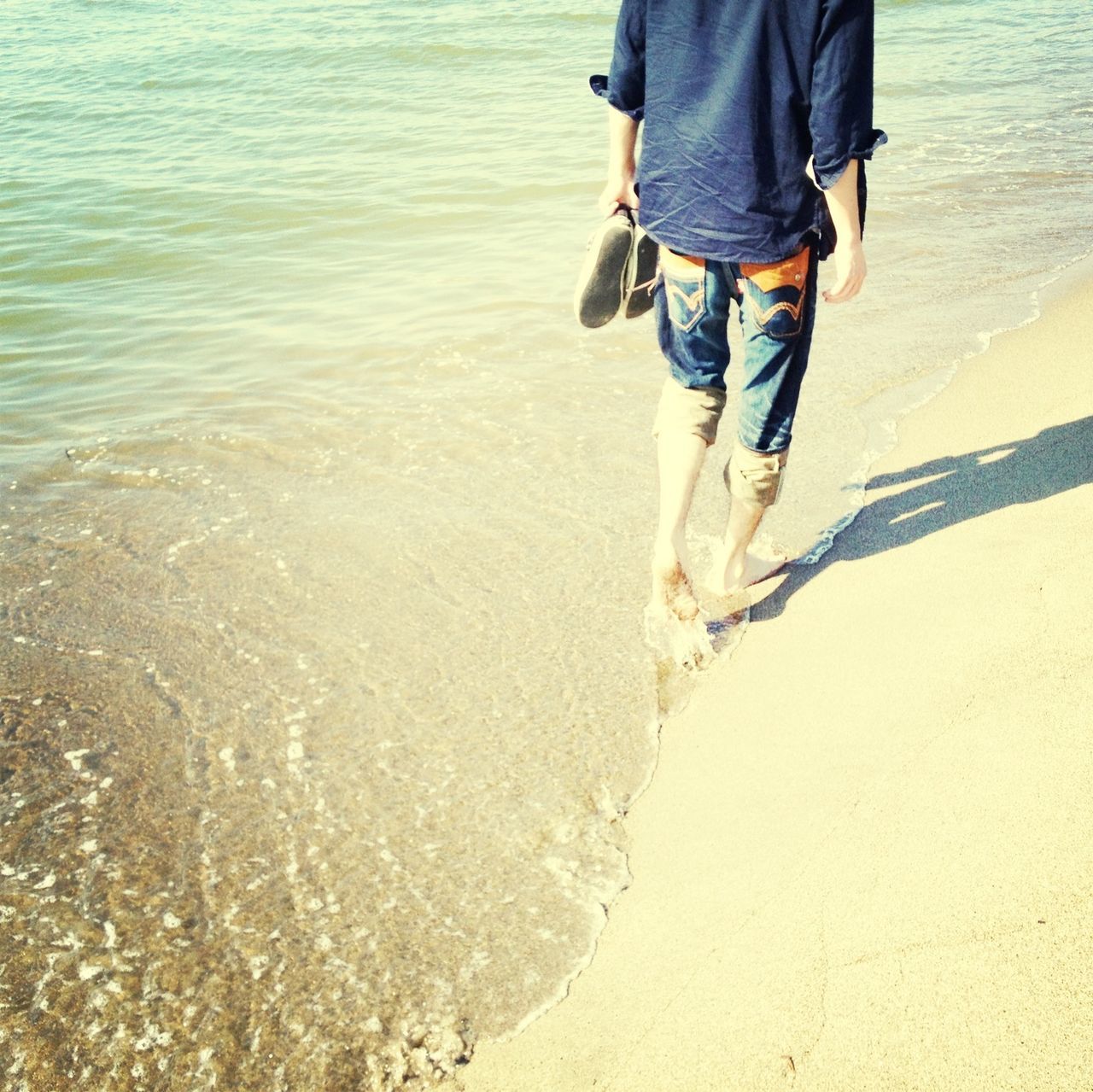 water, low section, beach, person, lifestyles, shore, sand, leisure activity, standing, men, sea, walking, sunlight, vacations, reflection, outdoors, high angle view