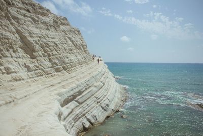 Rocky cliff by sea against sky