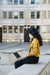 Businesswoman with face mask sitting outside working on laptop