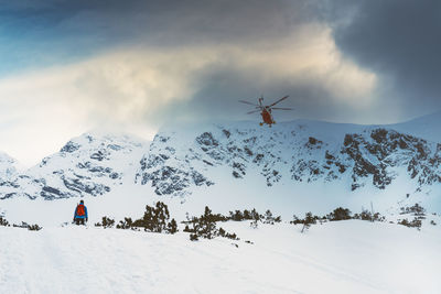 People skiing on snow covered landscape against sky during sunset