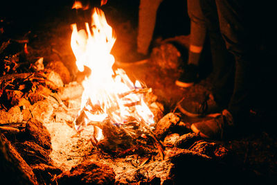 Low section of people standing by bonfire on field at night