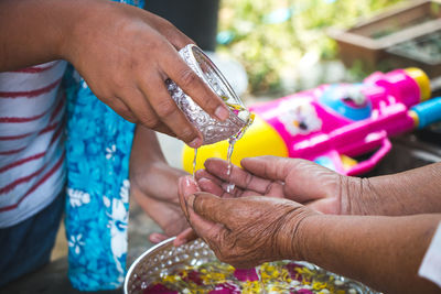 Midsection of woman pouring water on cropped hands 