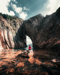 Rear view of person on rock by mountain against sky