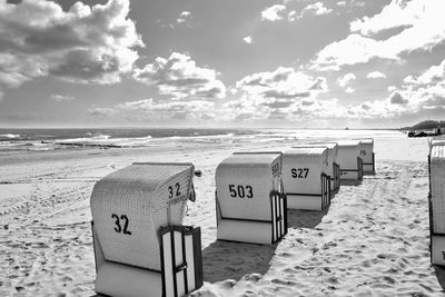 Hooded chairs on beach against sky