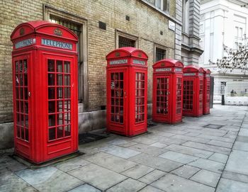 Red telephone booth on sidewalk by building in city