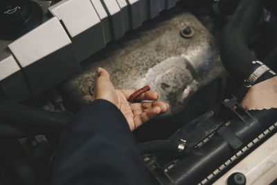 Cropped hand of mechanic examining oil in car engine at auto repair shop