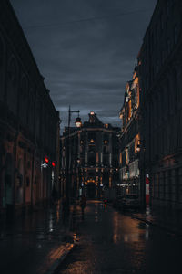 Wet street amidst buildings in city at night