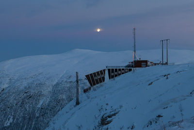 Overhead cable car station on snow covered mountain against sky at dusk