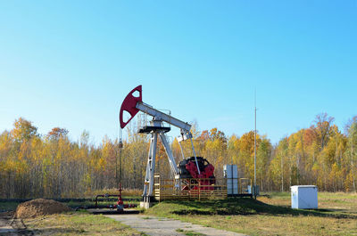 Traditional windmill on field by lake against clear blue sky