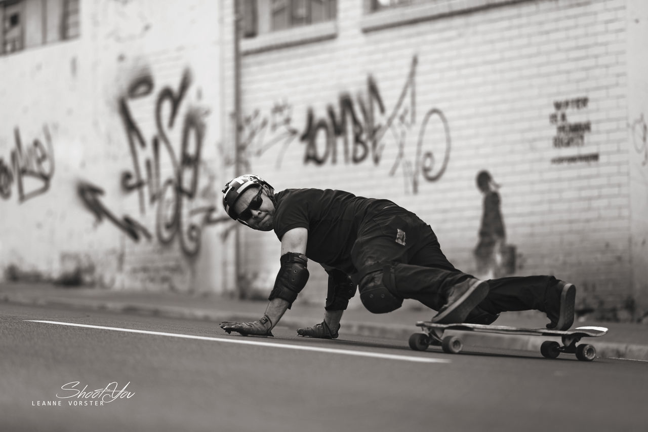 FULL LENGTH OF MAN SKATEBOARDING ON CITY IN BACKGROUND