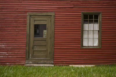 A crooked old door and window on the side of a dark red antique house in rural maine