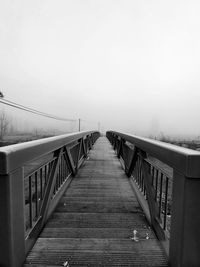 Wooden footbridge in fog against sky