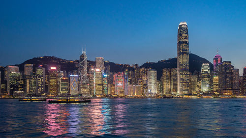 Illuminated buildings by river against sky at night