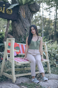 Portrait of young woman sitting on bench against tree