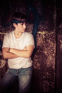 Young man looking away while sitting against wall