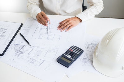 Midsection of engineer drawing on blueprint at table in office