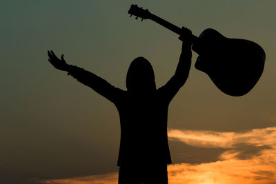 Silhouette man holding guitar against sky during sunset