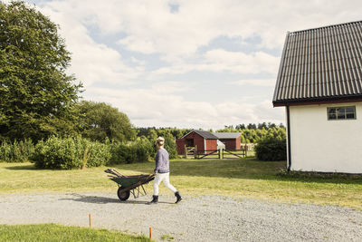 Farm worker with wheelbarrow walking on road by barn