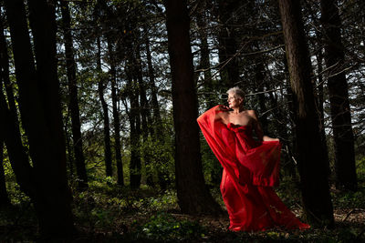 Senior woman with red scarf standing by trees in forest