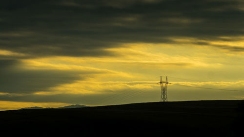Silhouette electricity pylon on land against sky during sunset