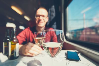 Portrait of mid adult man with wineglass on table sitting in train