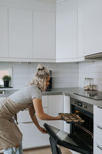 Woman in kitchen putting cupcakes in oven