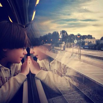 Cropped image of boy looking out through train window during sunset
