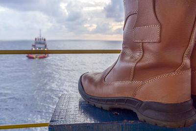 Close-up of boots at beach against sky