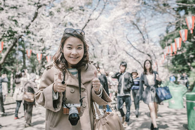 Portrait of smiling young woman standing against trees in city