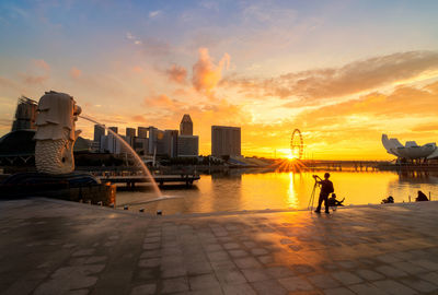 Rear view of man standing in city against sky during sunset