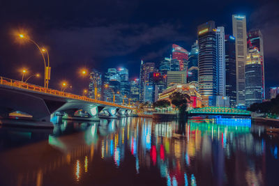 Illuminated bridge over river by buildings against sky at night