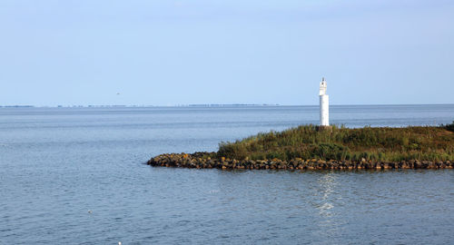 Lighthouse by sea against clear sky