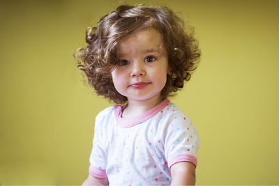 Portrait of cute baby girl standing against yellow background