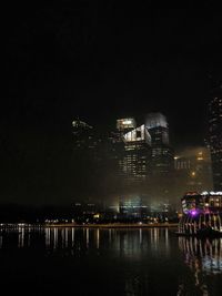 Illuminated city by river against sky at night