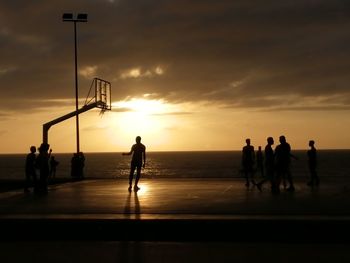 Silhouette people playing on beach against sky during sunset