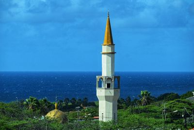 Lighthouse amidst buildings by sea against sky