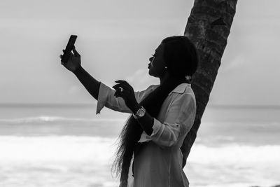 Africa woman from ghana is standing by phone in hand by the sea in axim ghana.