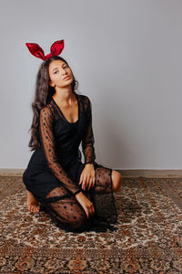 Young woman looking away while sitting on floor against wall