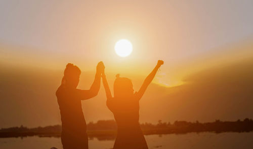 Silhouette friends standing against bright sun during sunset