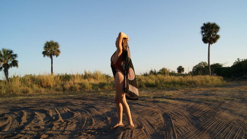 Side view full length of young woman wearing one piece swimsuit holding scarf on sand