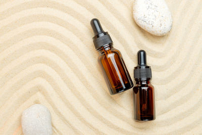 Dark glass bottles of moisturizing face serum, cosmetic oil and pebble stones on a sandy background