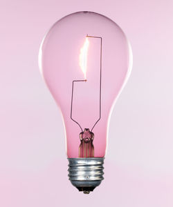 Close-up of illuminated light bulb against pink background