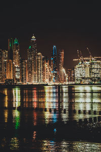 Illuminated buildings by river against sky at night