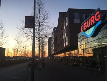 Road by buildings against sky during sunset in city