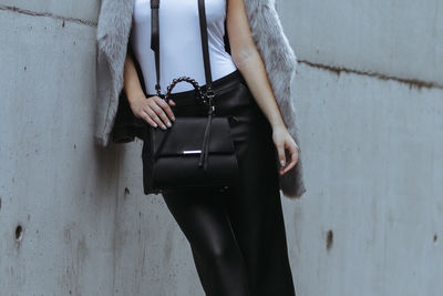 Midsection of woman holding umbrella standing against wall