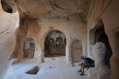 Side view of tourist sitting in cliff dwelling at zelve monastery