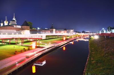 Illuminated bridge over river by buildings in city at night