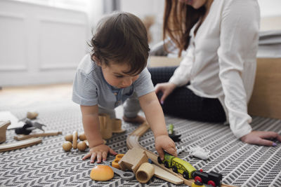 Baby boy playing with miniature train by mother on rug at home